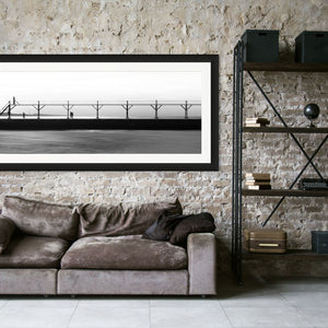 A couple strolls along The Pier in Black and White, with a bird flying nearby and a smokestack in the distance.